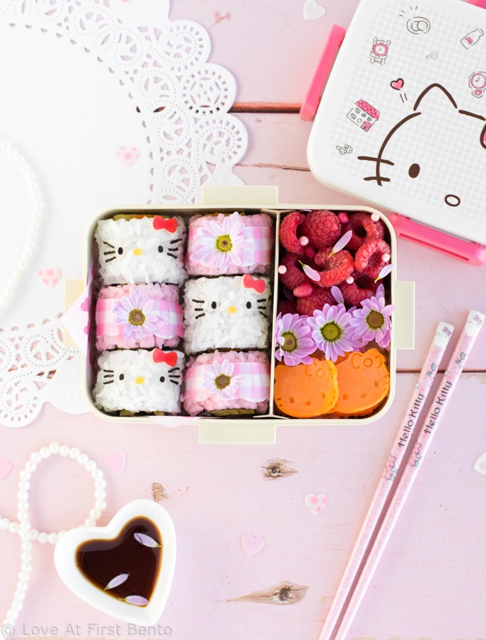 Hello Kitty Sushi Bento - Beautify your lunch with this Hello Kitty Sushi Bento! Filled with adorable Hello Kitty sushi rolls, as well as pink gingham flower sushi rolls, this pretty bento box is an edible dream come true for any Hello Kitty fan! Find out just how easy it is to make by visiting loveatfirstbento.com [character bento, kyaraben, deco sushi]