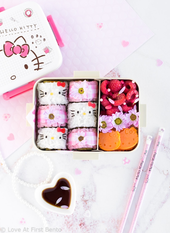 Hello Kitty Sushi Bento - Beautify your lunch with this Hello Kitty Sushi Bento! Filled with adorable Hello Kitty sushi rolls, as well as pink gingham flower sushi rolls, this pretty bento box is an edible dream come true for any Hello Kitty fan! Find out just how easy it is to make by visiting loveatfirstbento.com [character bento, kyaraben, deco sushi]